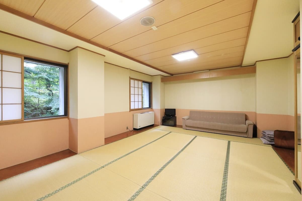 Une pièce avec un sol recouvert de tatamis, un canapé, un radiateur et une fenêtre donnant sur un paysage verdoyant.