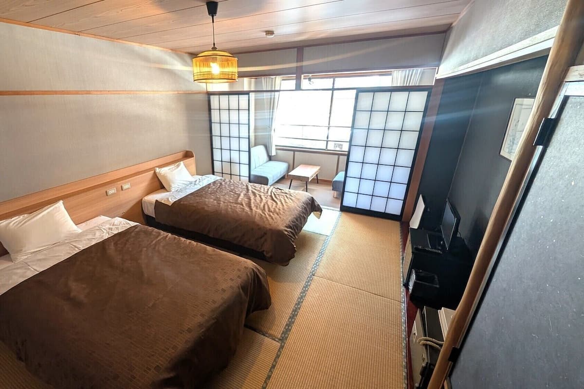 Une chambre d’hôtel avec deux lits, un sol recouvert de tatamis, une porte coulissante de style japonais traditionnel et un téléviseur.