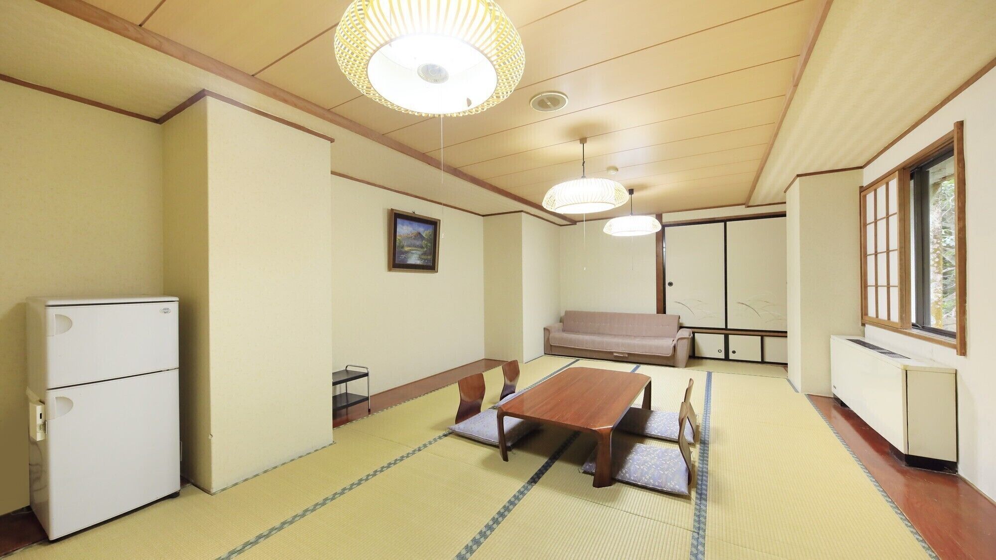 A traditional Japanese room with tatami flooring, a low table, a sofa, a refrigerator, and sliding doors.