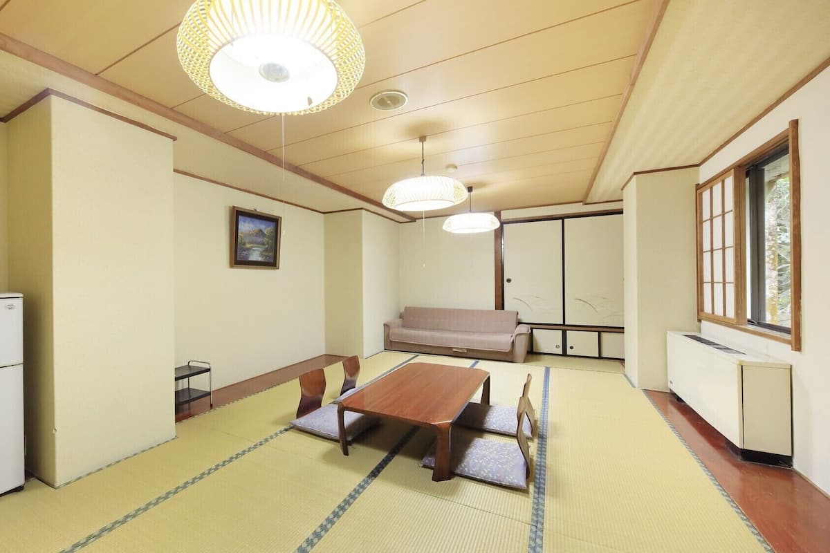 Une pièce de style japonais traditionnel, avec un sol recouvert de tatamis, une table basse, un canapé, un réfrigérateur et des portes coulissantes.