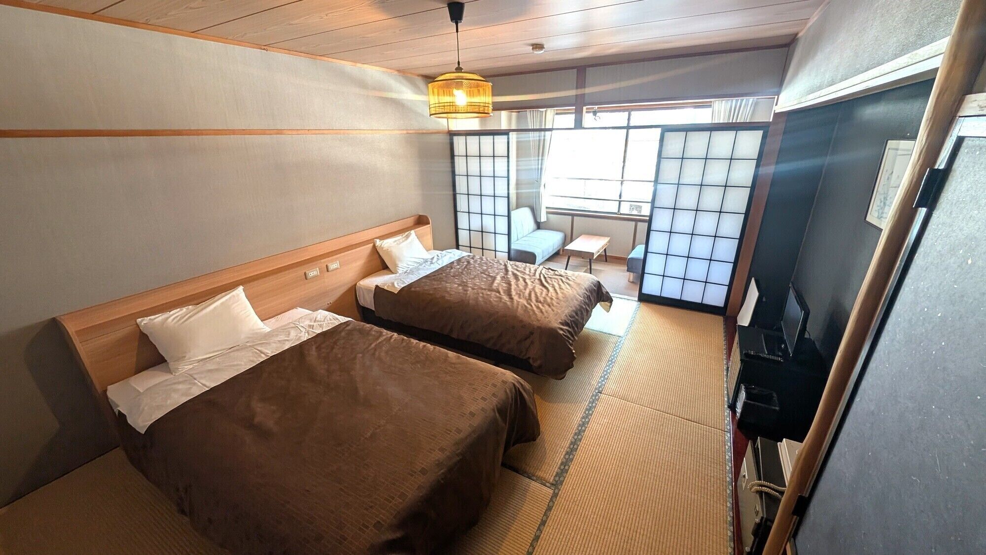 A hotel room with two beds, a tatami mat floor, a traditional Japanese sliding door, and a small table.