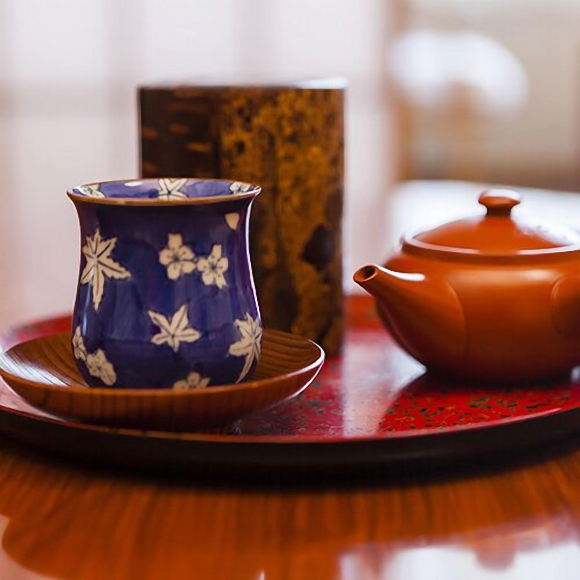A ceramic cup with floral patterns, a teapot, and a wooden box on a table.