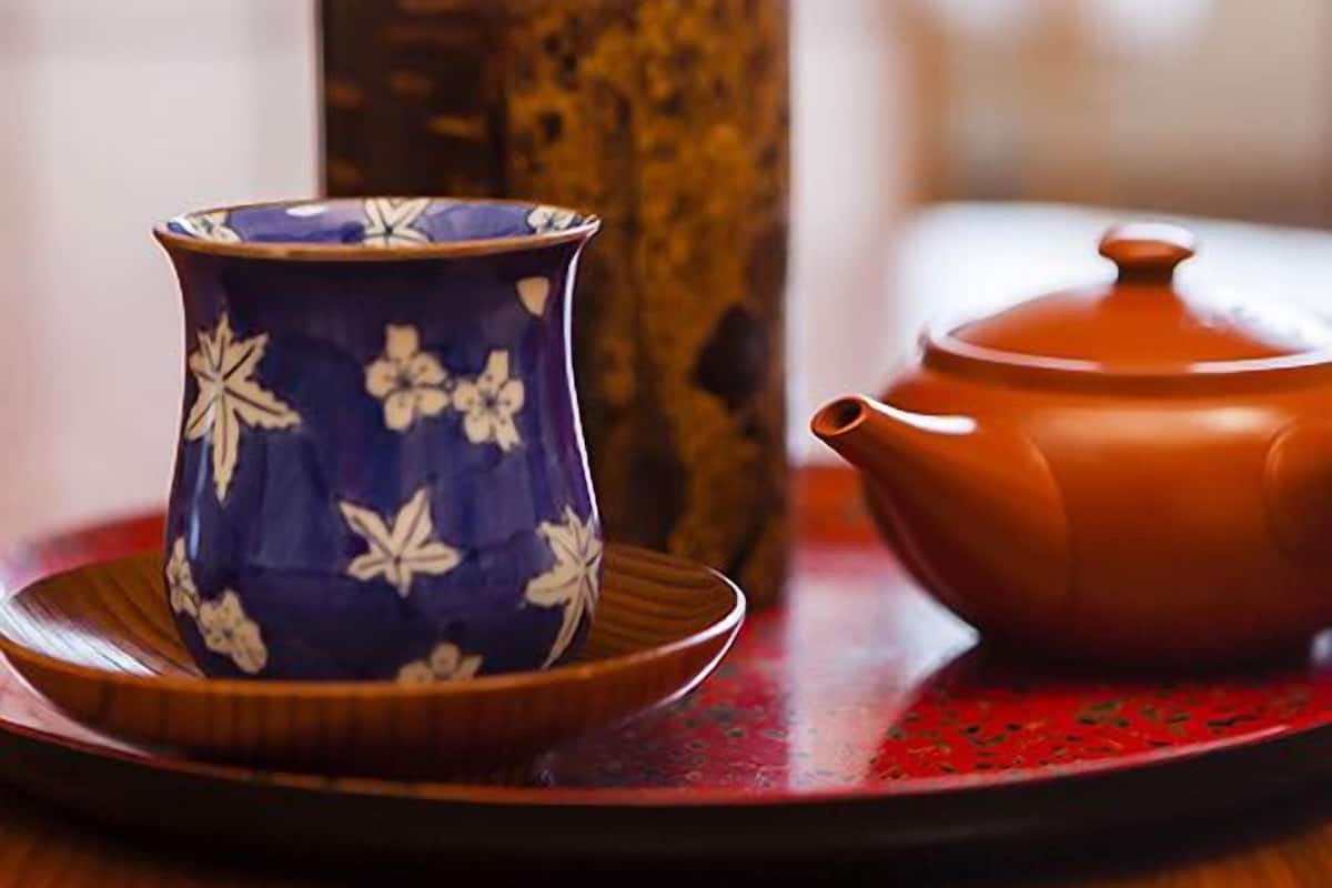 Une tasse en céramique ornée de motifs floraux, une théière et une boîte en bois, le tout posé sur une table.