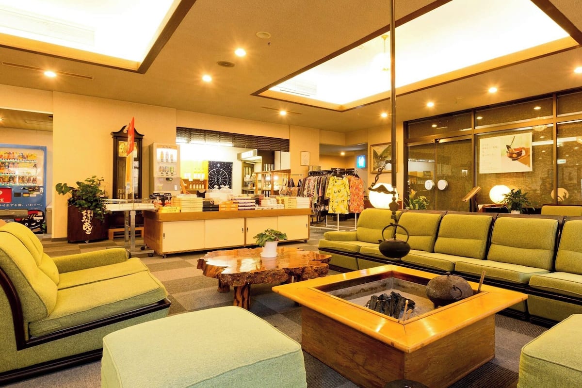 Un hall d’hôtel comprenant un canapé, des fauteuils, une table basse, un comptoir d’accueil et une boutique de vêtements.