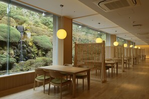 A restaurant with a view of a waterfall and lush greenery, wooden furniture, and pendant lighting. - Senkyoro (Hakone)