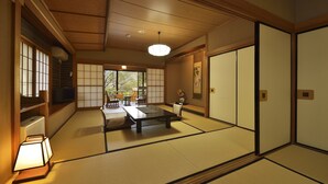 Une pièce de style japonais traditionnel, avec un sol recouvert de tatamis, une table basse avec des coussins, des portes coulissantes et un luminaire suspendu.