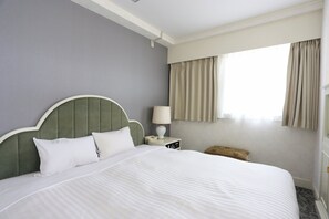 A neatly made bed with white linens, a green upholstered headboard, a bedside table with a lamp, and a window with curtains. - Hotel Castle inn Yokkaichi (Yokkaichi)