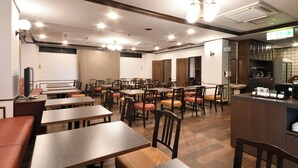 Ein Hotelrestaurant mit mehreren Tischen, Stühlen, einer Bar und einer Küche im Hintergrund.