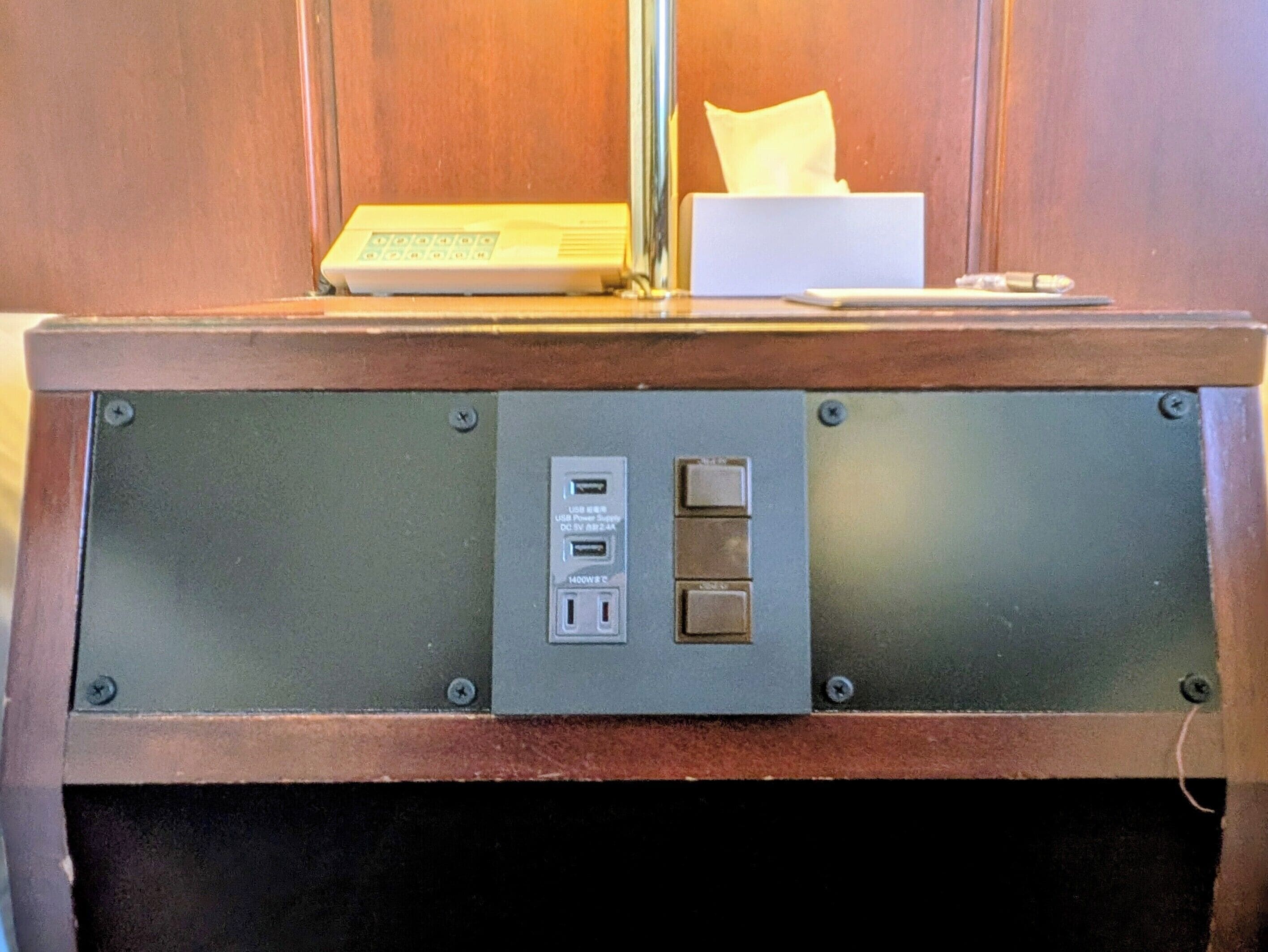 Un panneau de commande doté de ports USB et d’une prise électrique, une boîte à mouchoirs et une télécommande, le tout posé sur une surface en bois.