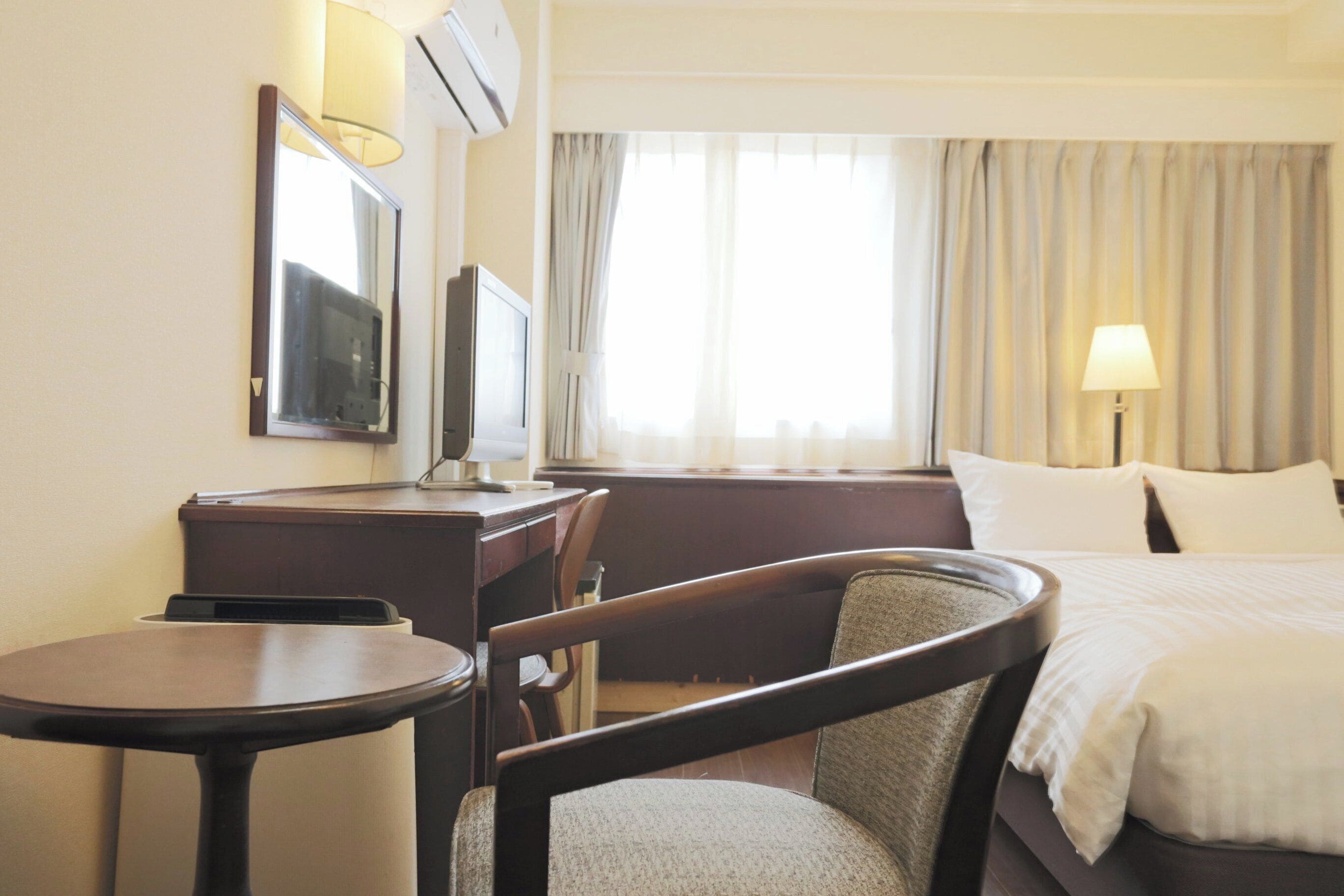 A hotel room with a bed, a desk, a chair, a television, and a window with curtains.