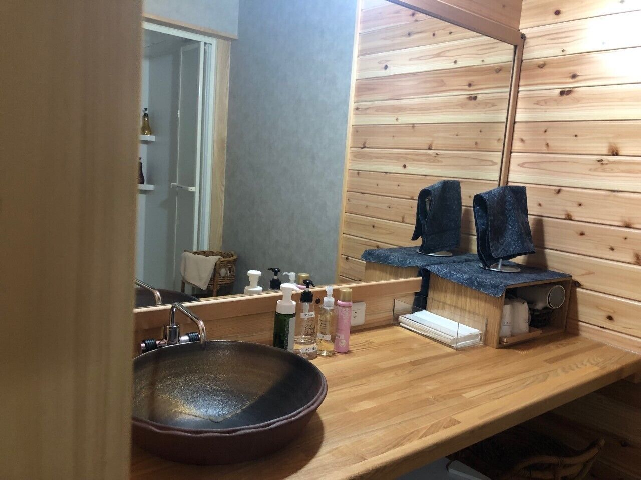 A bathroom with a wooden vanity, a large mirror, a sink, and shelves with toiletries.