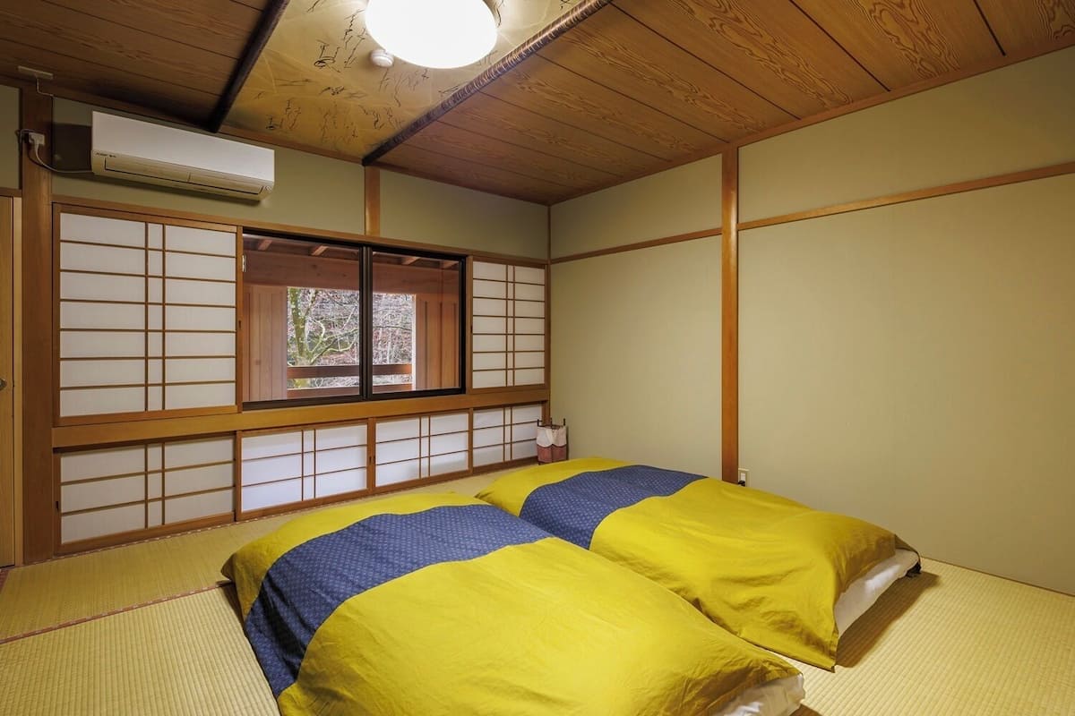 Ein traditioneller japanischer Raum mit Tatami-Bodenbelag, Futon-Bett, Shoji-Bildschirmen und Deckenventilator.