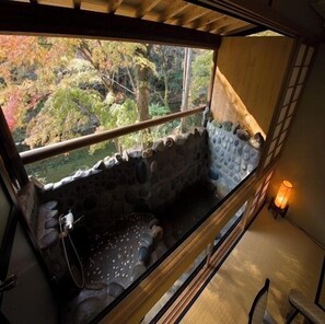 A stone bath with a view of autumn trees, a wooden bench, and a wall-mounted lamp. - Sengakukan (Gero)