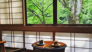 Una habitación tradicional con suelo de tatami, una mesa baja con juego de té y un ventanal con vistas a un bosque.