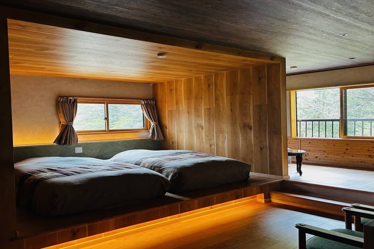 Ein Holzhüttenraum mit Bett, Fenstern und Blick ins Freie.