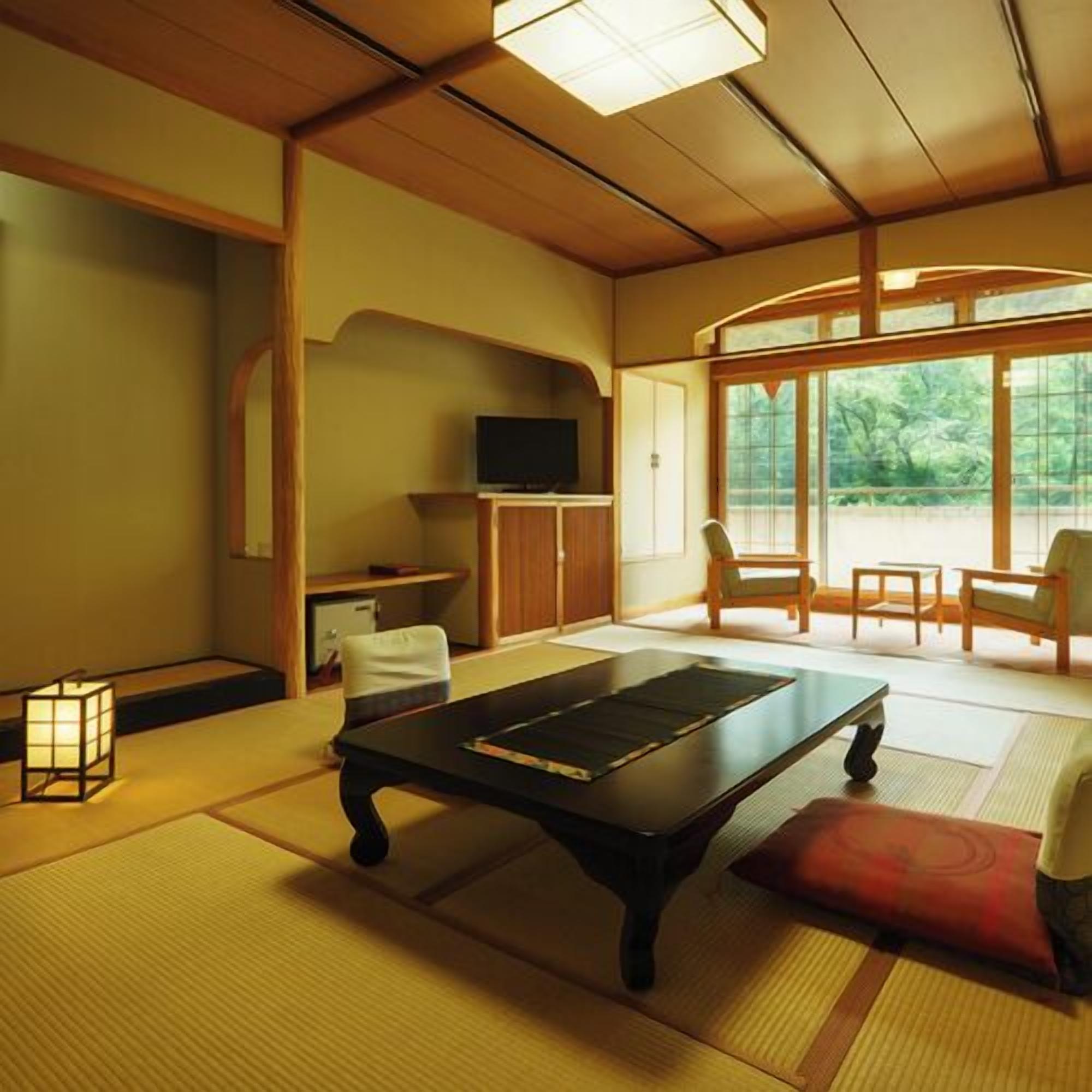 A traditional Japanese-style room with tatami flooring, a low table, a television, and a view of greenery outside.