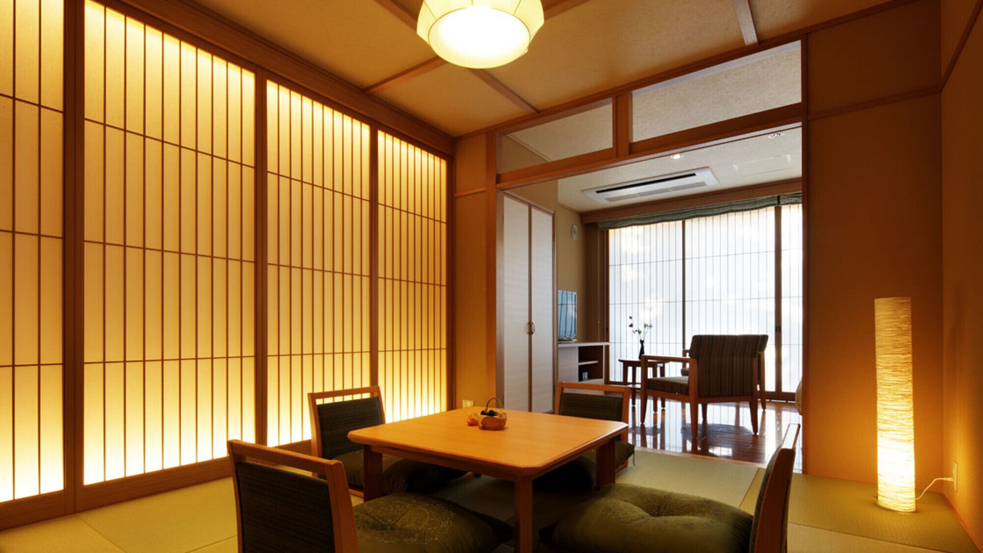 A traditional Japanese-style room with tatami flooring, sliding shoji doors, a low table with chairs, and a standing lamp.