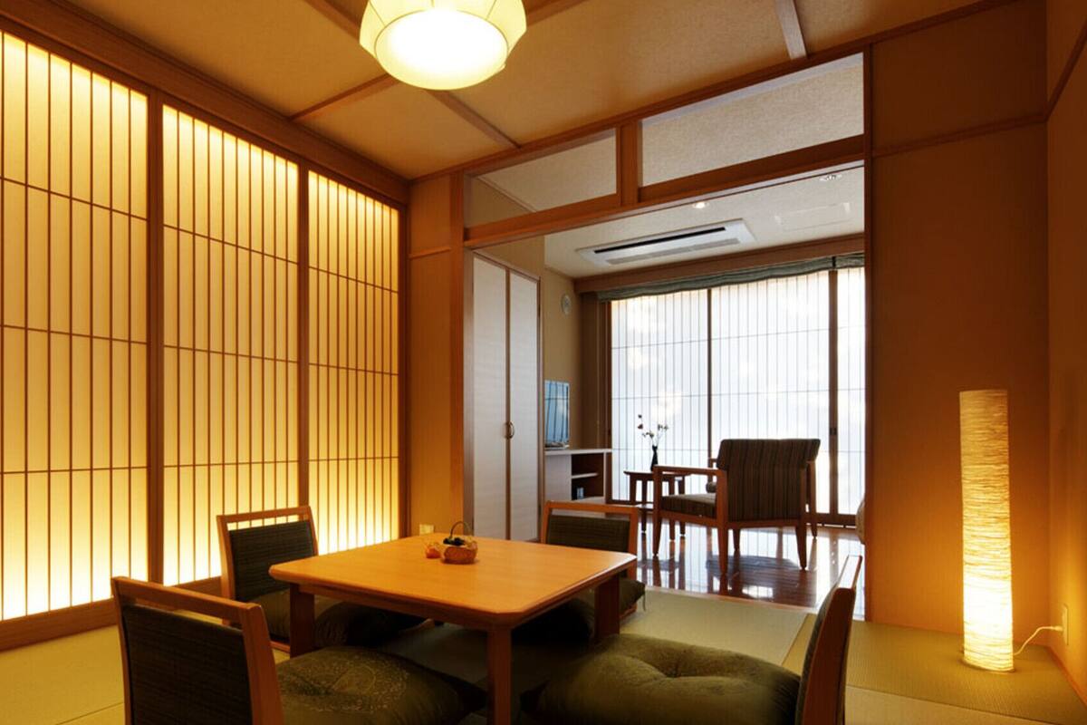 Una habitación tradicional japonesa con suelo de tatami, puertas correderas shoji, una mesa baja con sillas y una lámpara de pie.