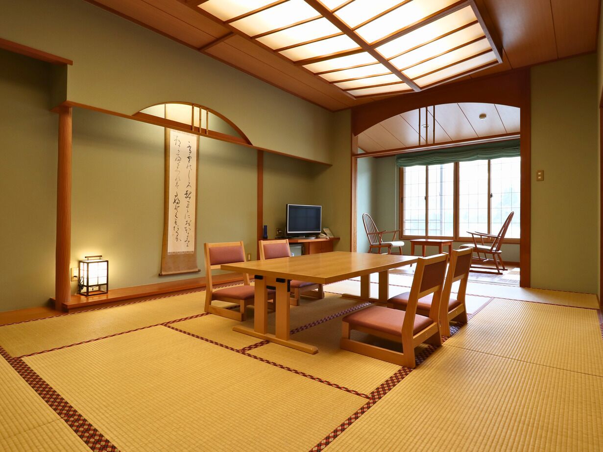 Una habitación japonesa tradicional con suelo de tatami, una mesa de madera, sillas, un televisor y un divisor shoji.