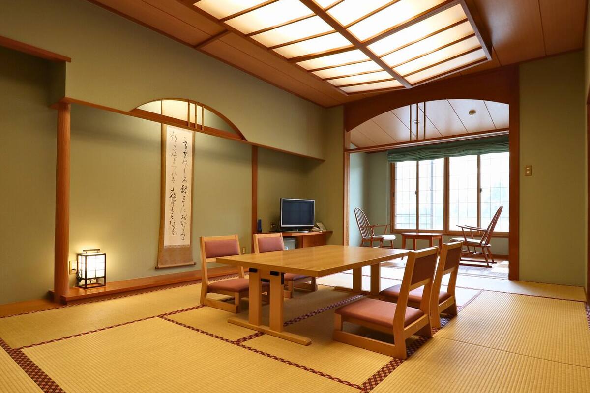 Una habitación japonesa tradicional con suelo de tatami, una mesa de madera, sillas, un televisor y un divisor shoji.
