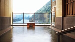 A room with a large window overlooking a river and mountains, a wooden bench, and a tiled floor.