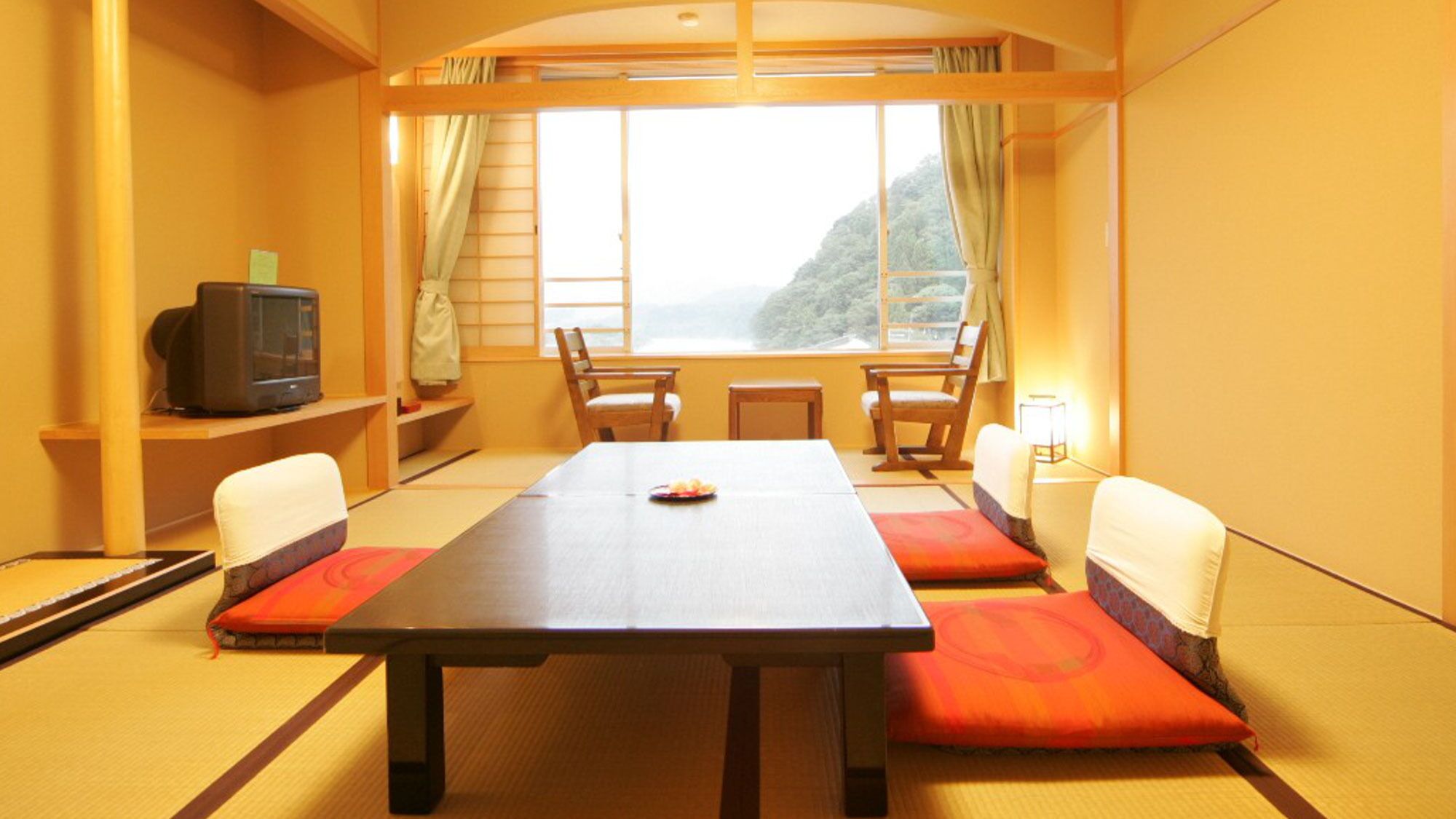 Una habitación con una mesa grande, dos sillas, un televisor y vistas a la montaña.
