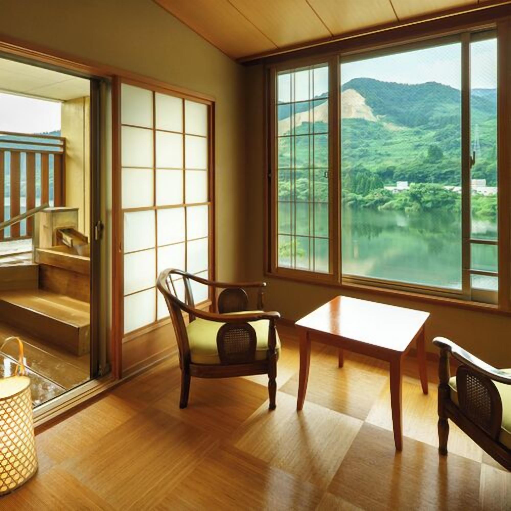 Una habitación con vistas a un lago y montañas, suelo de madera, una mesa y una silla.