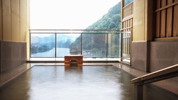 A room with a large window, a wooden bench, and a view of a river and mountains.