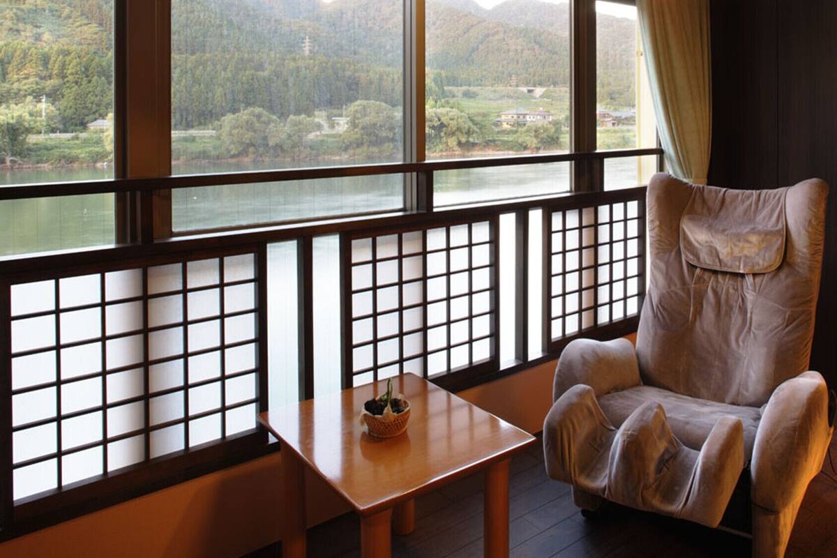 Una habitación con vistas a un lago y montañas, un sillón mullido, una mesita con una cesta y una lámpara de pie.