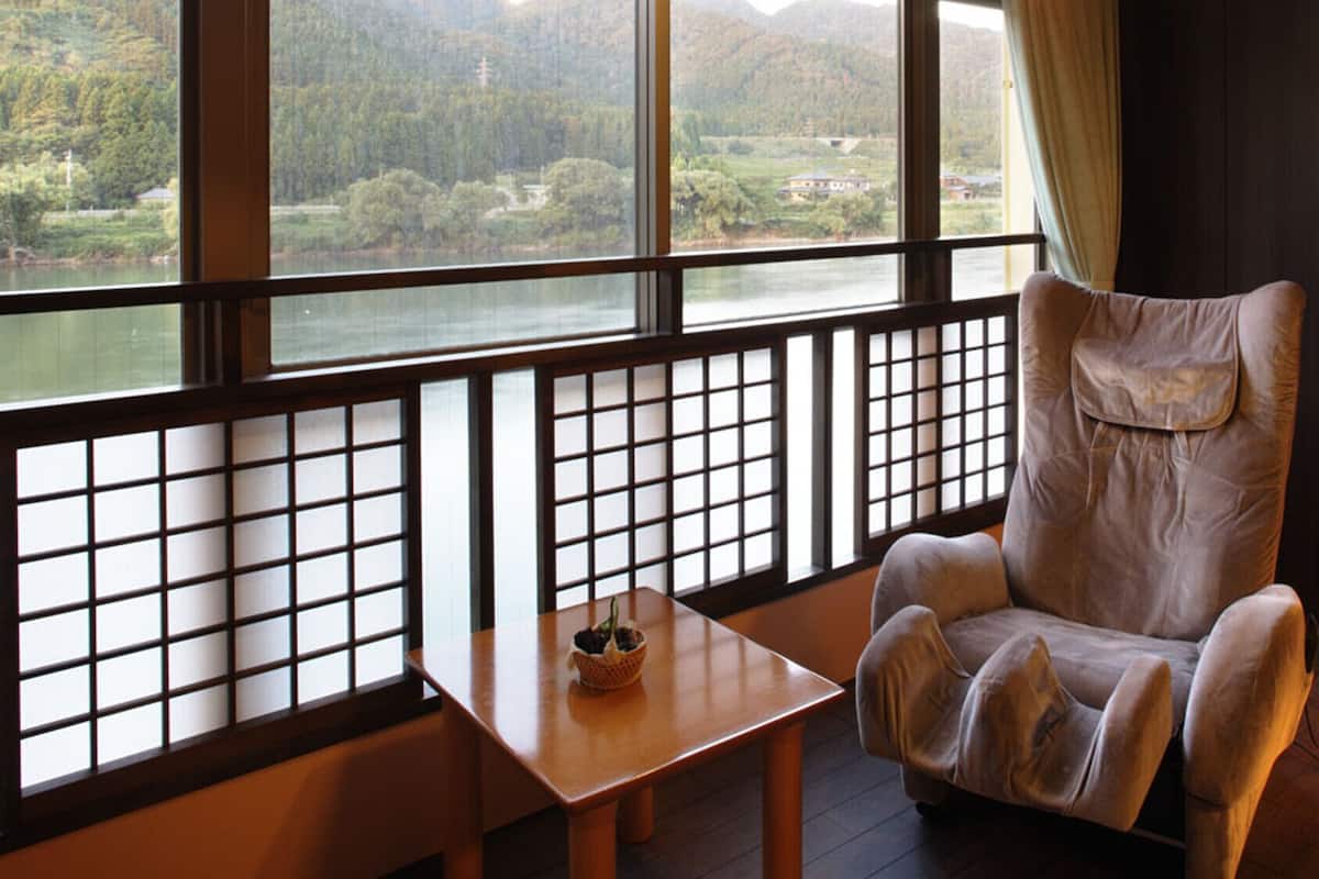 Una habitación con vistas a un lago y montañas, un sillón mullido, una mesita con una cesta y una lámpara de pie.