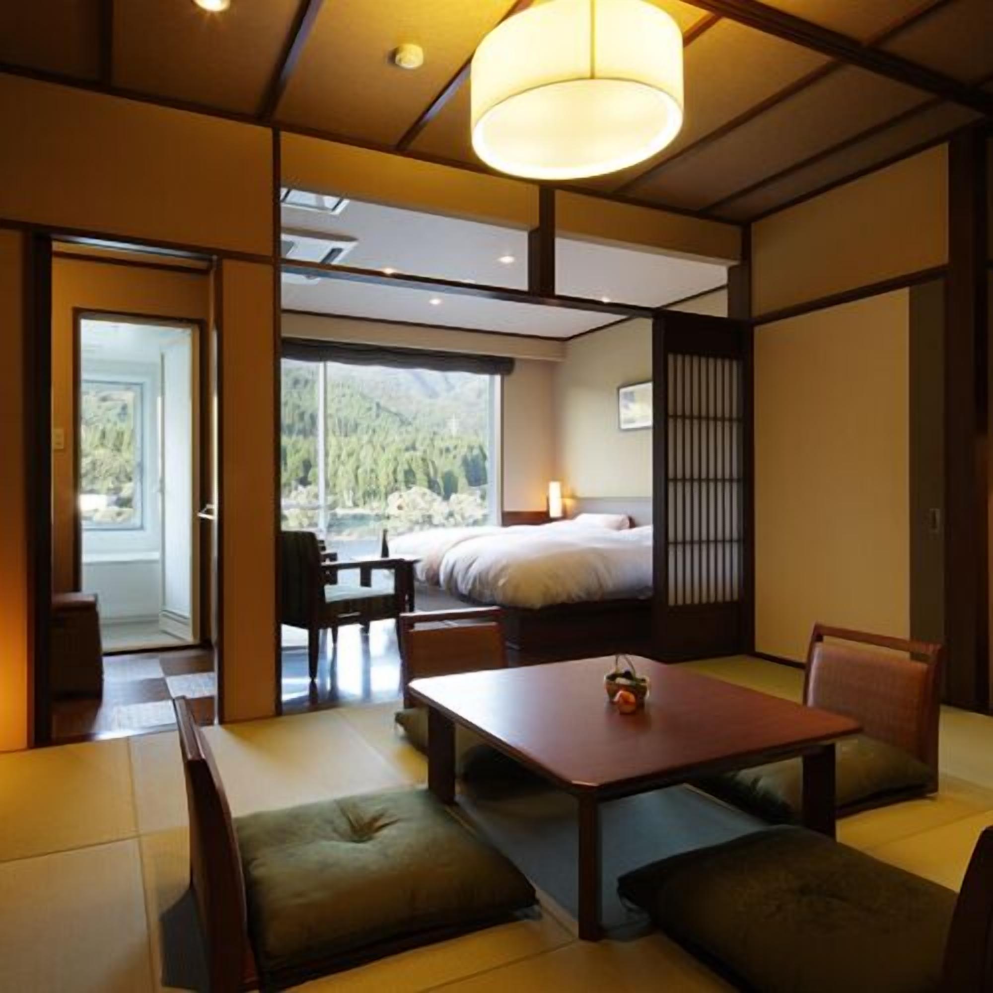 A traditional Japanese-style room with tatami flooring, a low table, cushions, and a bed with a view of the outdoors.
