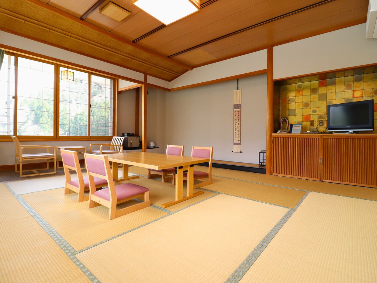 Una habitación japonesa tradicional con suelo de tatami, una mesa de madera baja con sillas, un televisor y un mueble con un salpicadero de azulejos.