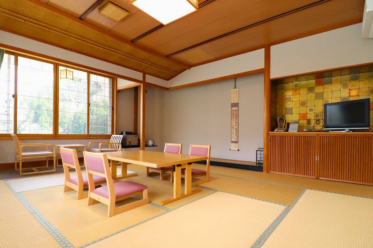 Una habitación japonesa tradicional con suelo de tatami, una mesa de madera baja con sillas, un televisor y un mueble con un salpicadero de azulejos.