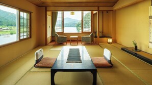 A traditional Japanese room with tatami flooring, a low table, two chairs, a view of a lake, and a small table with a lantern.