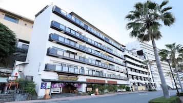 Um hotel com vários andares, varandas, entrada tradicional e palmeiras.