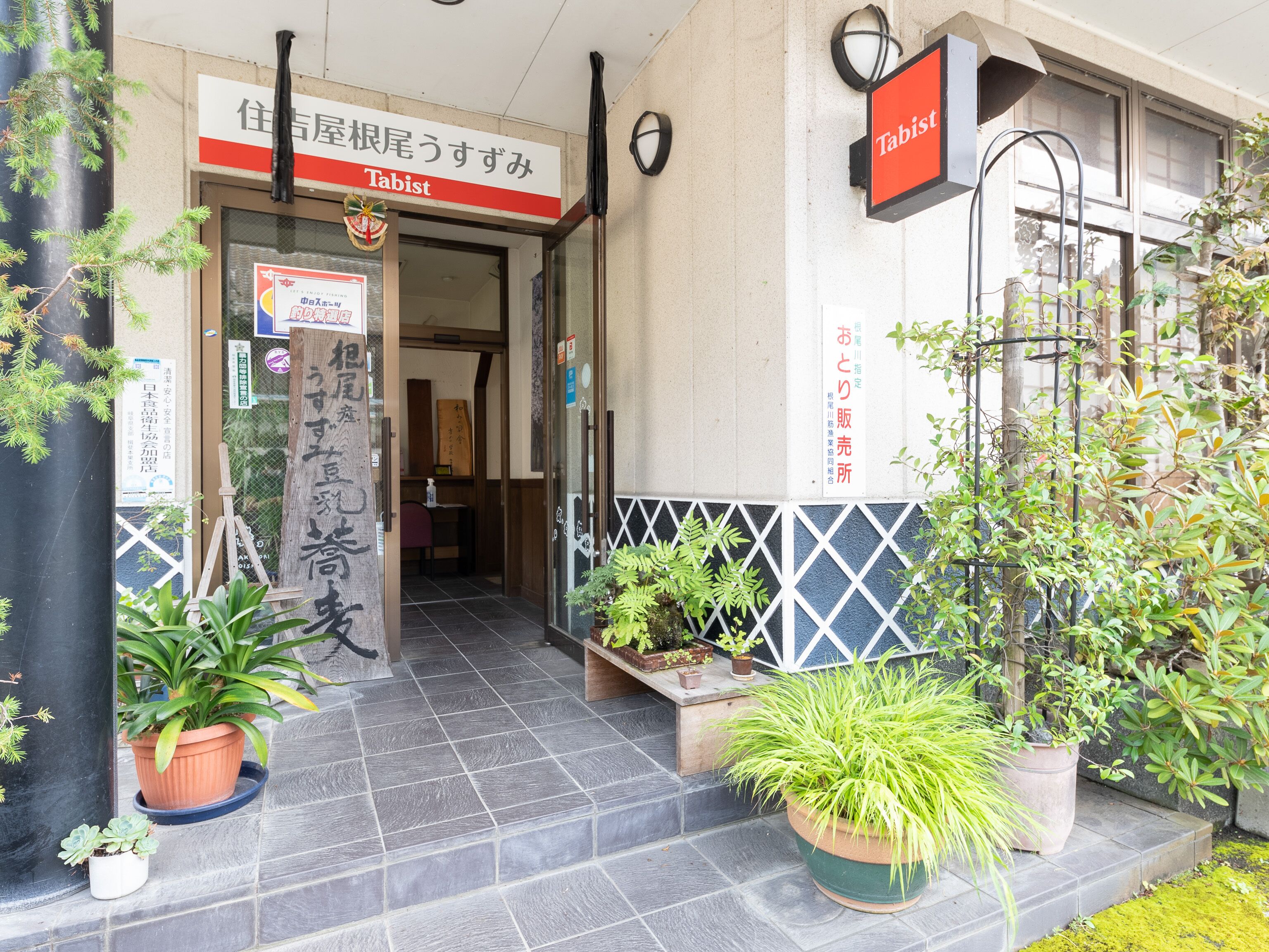 A hotel entrance with a sign reading "Tabist" and Japanese text. There are potted plants in front of the entrance.