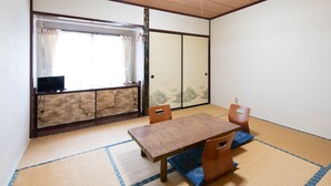 Una habitación japonesa tradicional con suelo de tatami, una mesa de madera baja y un puertas correderas con vistas a un jardín.