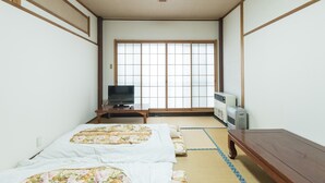 Una habitación japonesa tradicional con suelo de tatami, futón, televisor y calefactor.
