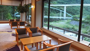 A traditional Japanese-style room with tatami flooring, wooden furniture, and large windows offering a view of a bridge and greenery. - Kashiwaya (Nikko)