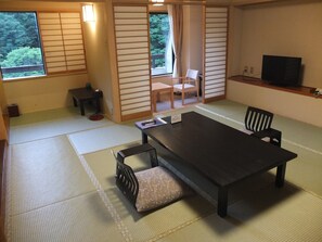 A traditional Japanese room with tatami flooring, a low table with cushions, a television on a shelf, and sliding doors with a view of greenery outside. - Kashiwaya (Nikko)