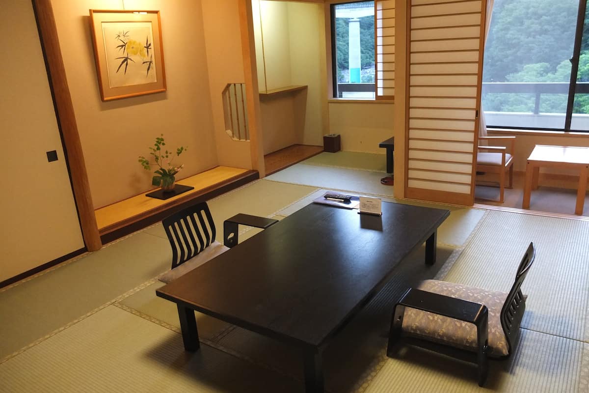 Una habitación japonesa tradicional con suelo de tatami, una mesa baja con un banco y una puerta corredera.