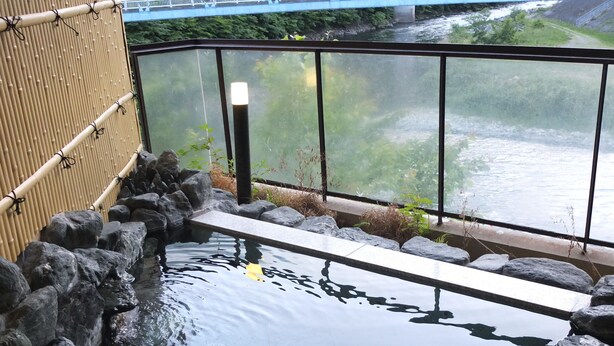 A tranquil indoor water feature with a stone border, a wooden bench, and a view of a bridge over a river. - Kashiwaya (Nikko)