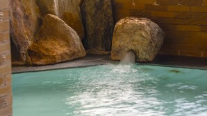 A pool with a water feature, surrounded by large rocks and a brick wall. - Chres (Kochi)