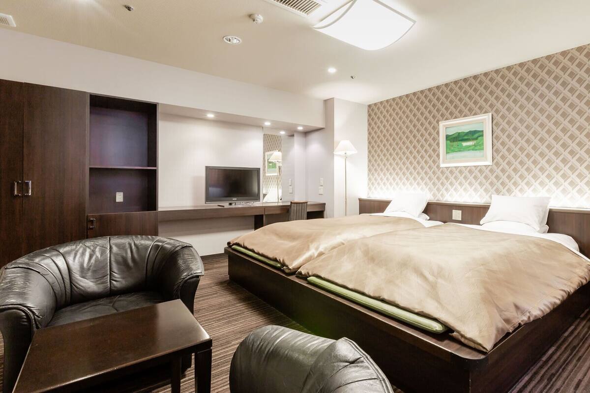 Une chambre d’hôtel comprenant un lit, deux chaises, un bureau, une télévision et un tableau accroché au mur.