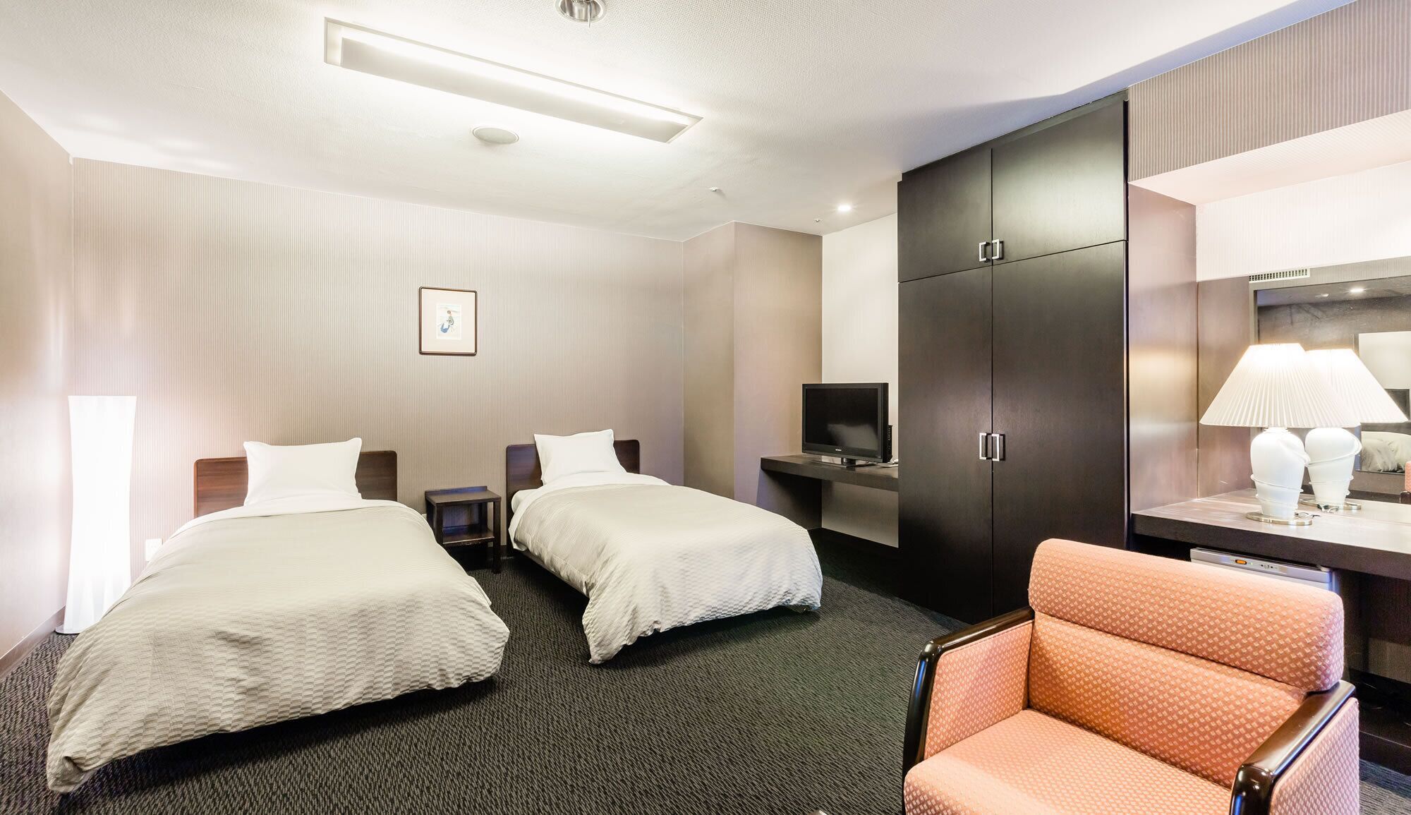 Une chambre d’hôtel avec deux lits, une télévision, une armoire, un bureau avec une lampe et une chaise.