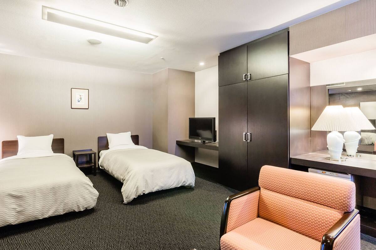 Une chambre d’hôtel avec deux lits, une télévision, une armoire, un bureau avec une lampe et une chaise.
