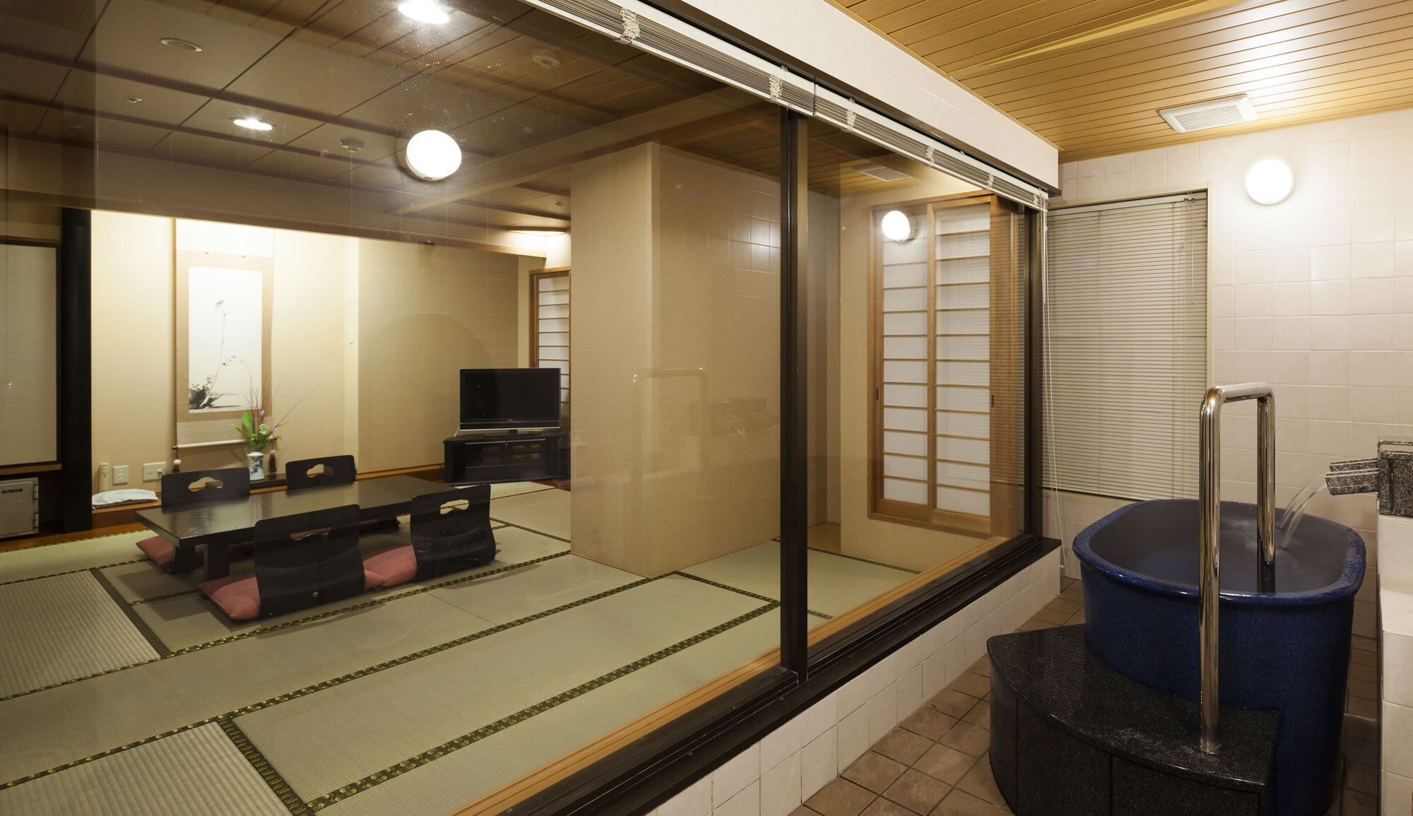 A traditional Japanese room with tatami flooring, a sliding door, a television, and a large blue water feature.