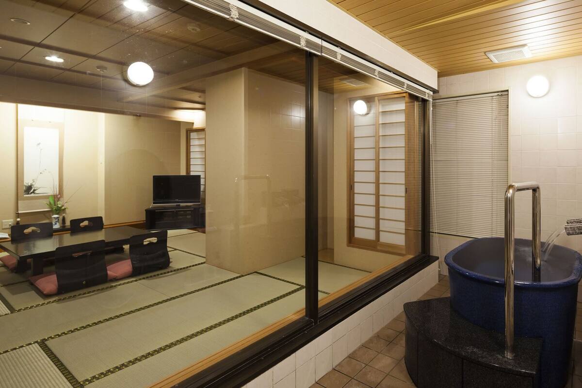 Une pièce de style japonais traditionnel, avec un sol recouvert de tatamis, une porte coulissante, un téléviseur et une grande fontaine bleue.