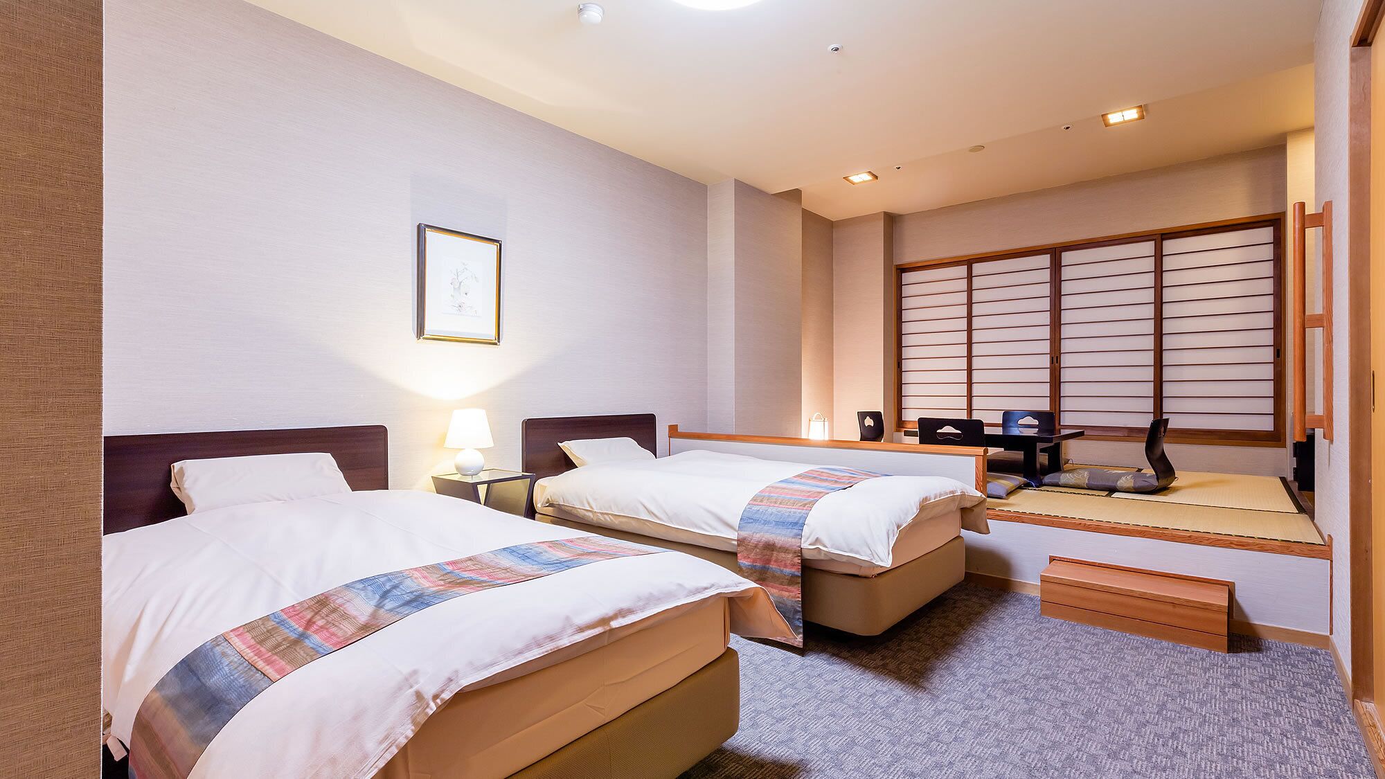 A hotel room with two beds, a desk, a chair, a tatami mat, and a shoji screen.