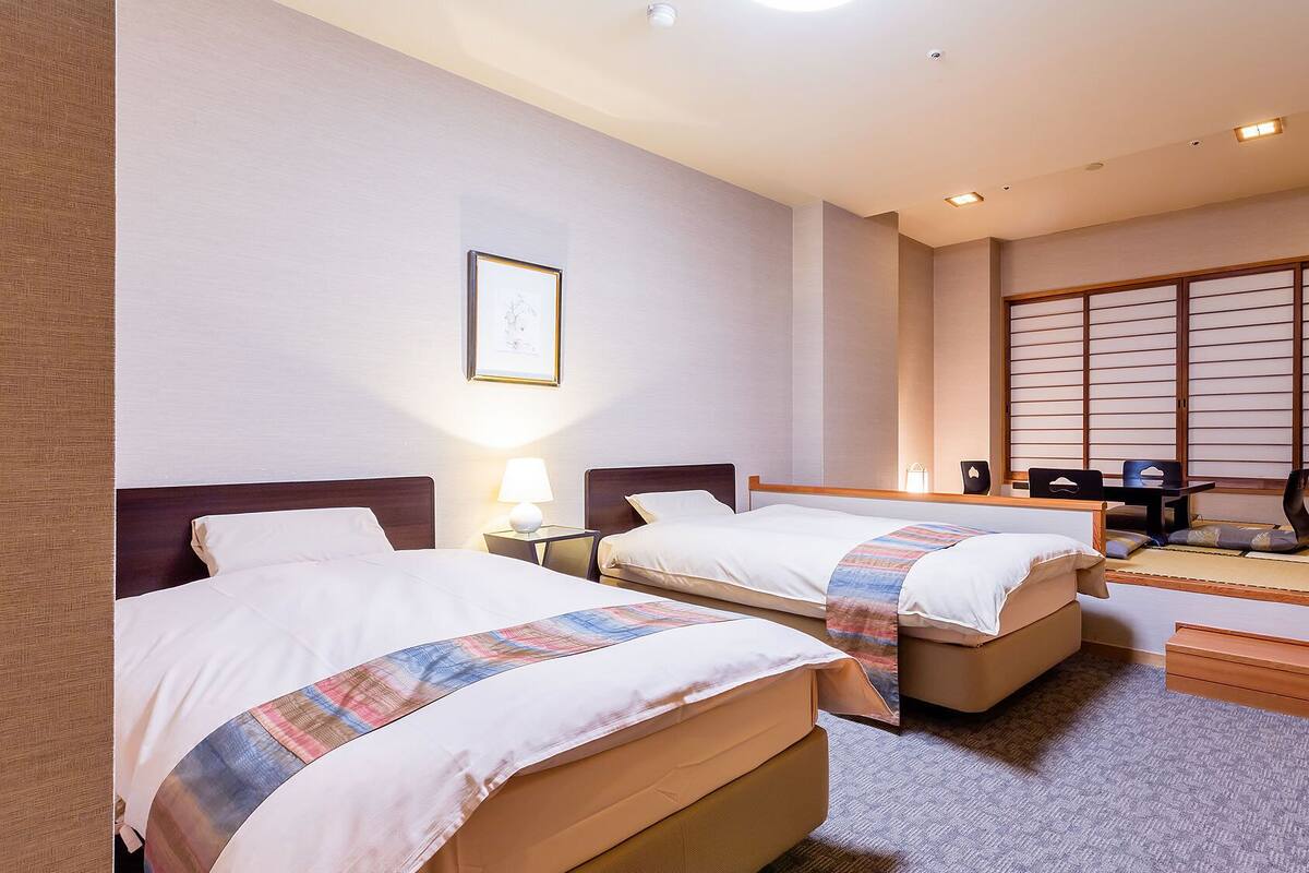 Une chambre d’hôtel avec deux lits, un bureau, une chaise, un tatami et un paravent en papier.